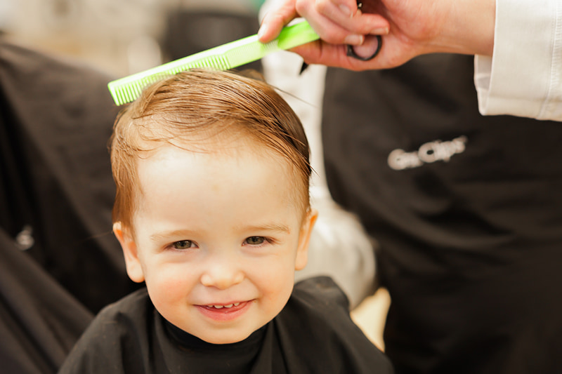 Smiling toddler sitting in a salon chair and enjoying a lollipop