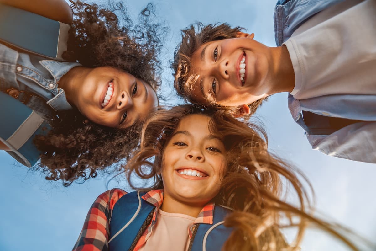 Three young kids in a huddle smiling down at the camera