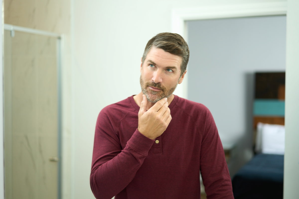 A man in a red shirt looking into a mirror and fixing his beard A man in a red shirt looking into a mirror and fixing his beard