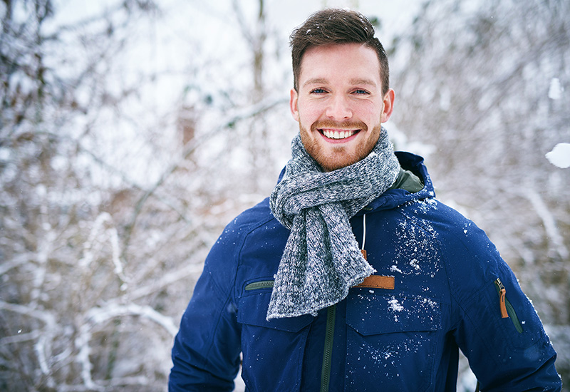 Man with short hair and a beard smiling and wearing a winter coat and scarf on a cold winter day