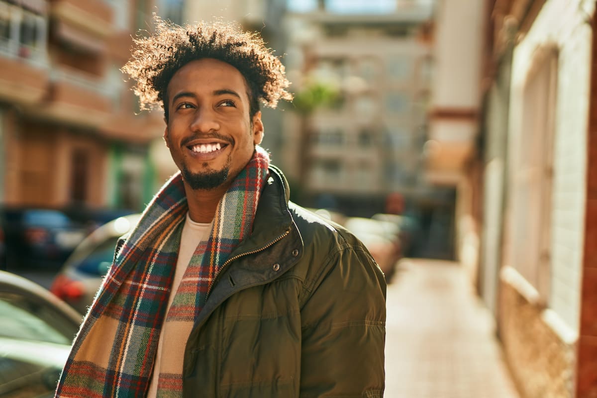 Man wearing coat and scarf smiling and walking down street Man wearing coat and scarf smiling and walking down street