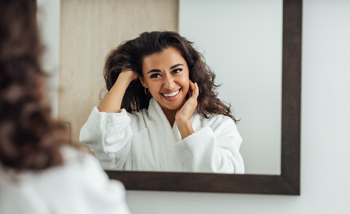 Woman smiling at herself in the mirror as she finger-combs her long hair