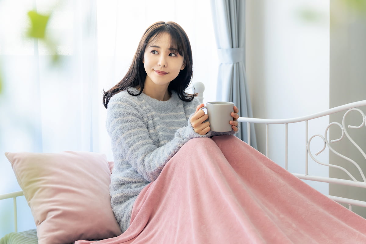 woman sitting under a blanket and holding a coffee cup woman sitting under a blanket and holding a coffee cup