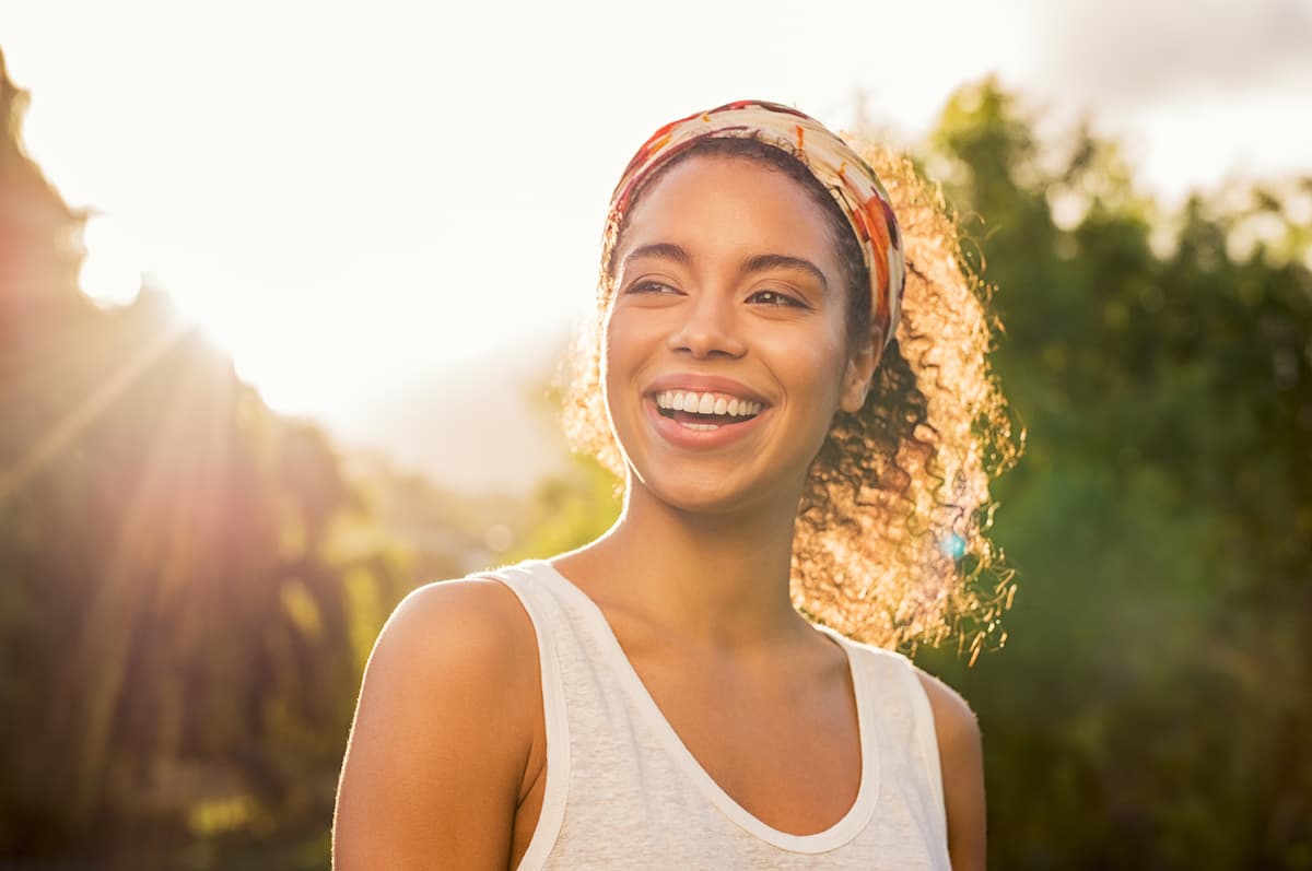 Woman with hair in a hairband standing outside in the summer sun and smiling