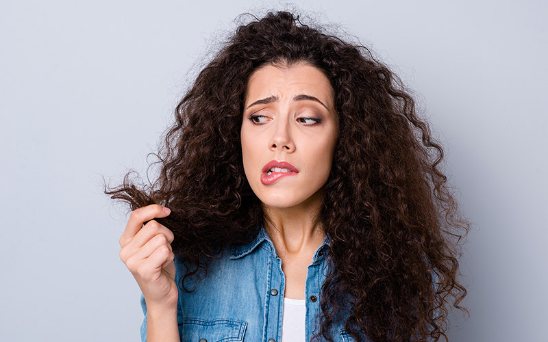 Woman with a worried expression looking closely at her dry curly hair