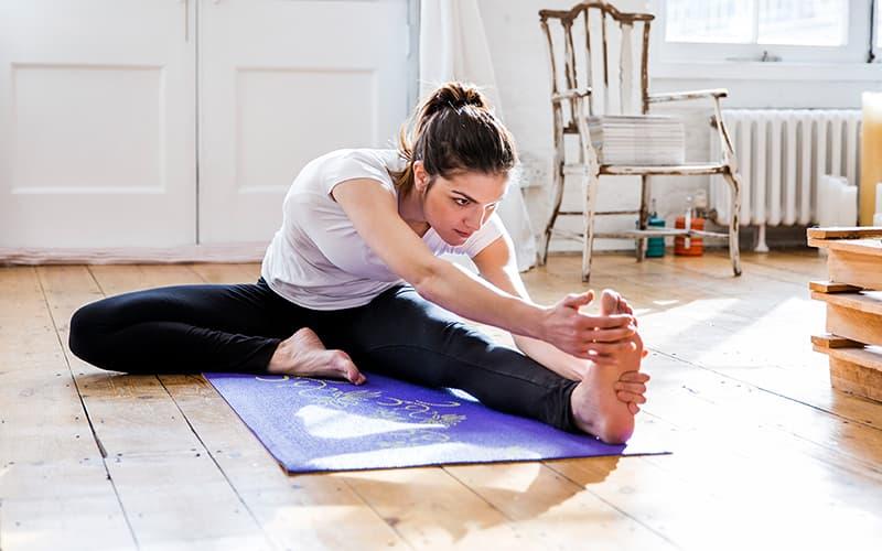 Woman with her hair in a ponytail stretching on a yoga mat