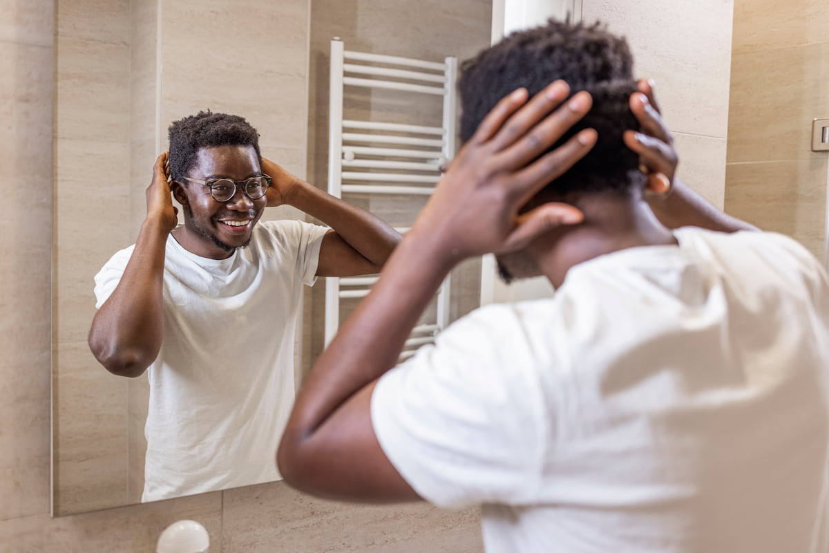 A man with glasses looking at his hair in a mirror. A man with glasses looking at his hair in a mirror.